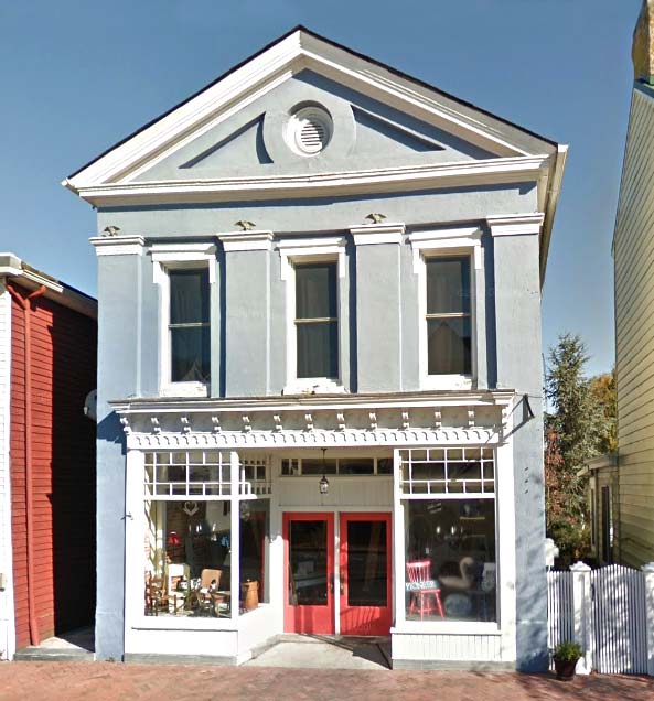 Image of Odd Fellows Hall in Smyrna, DE. A two-story, light blue building with a red front door and display windows on the first floor.